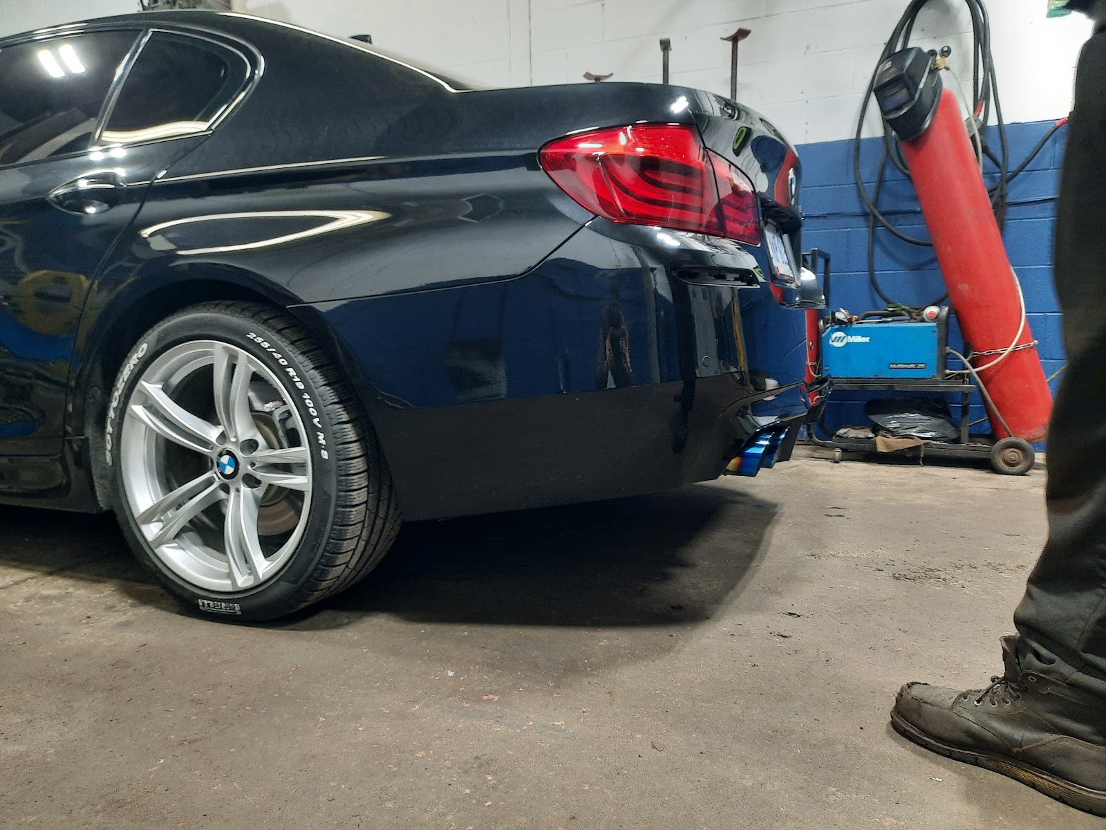 A dark BMW on the lift at Muffler Hut with a custom blue exhaust tip and welder on the bench